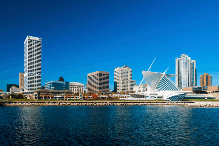 Milwaukee city skyline with modern and historic buildings, including the Milwaukee Art Museum, viewed from across the water on a clear day.