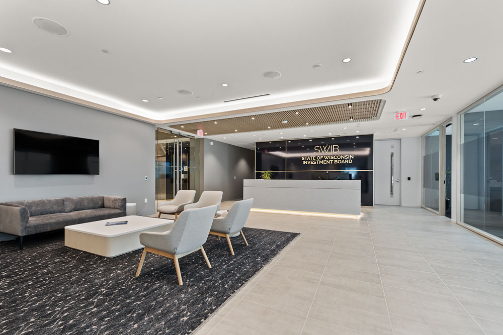 Modern office lobby with a reception desk labeled "State of Wisconsin Investment Board," seating area, TV, and neutral-toned decor.