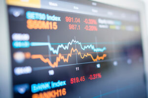 Close-up of a digital screen displaying fluctuating stock market indexes in red and blue, with numerical values and percentage changes.